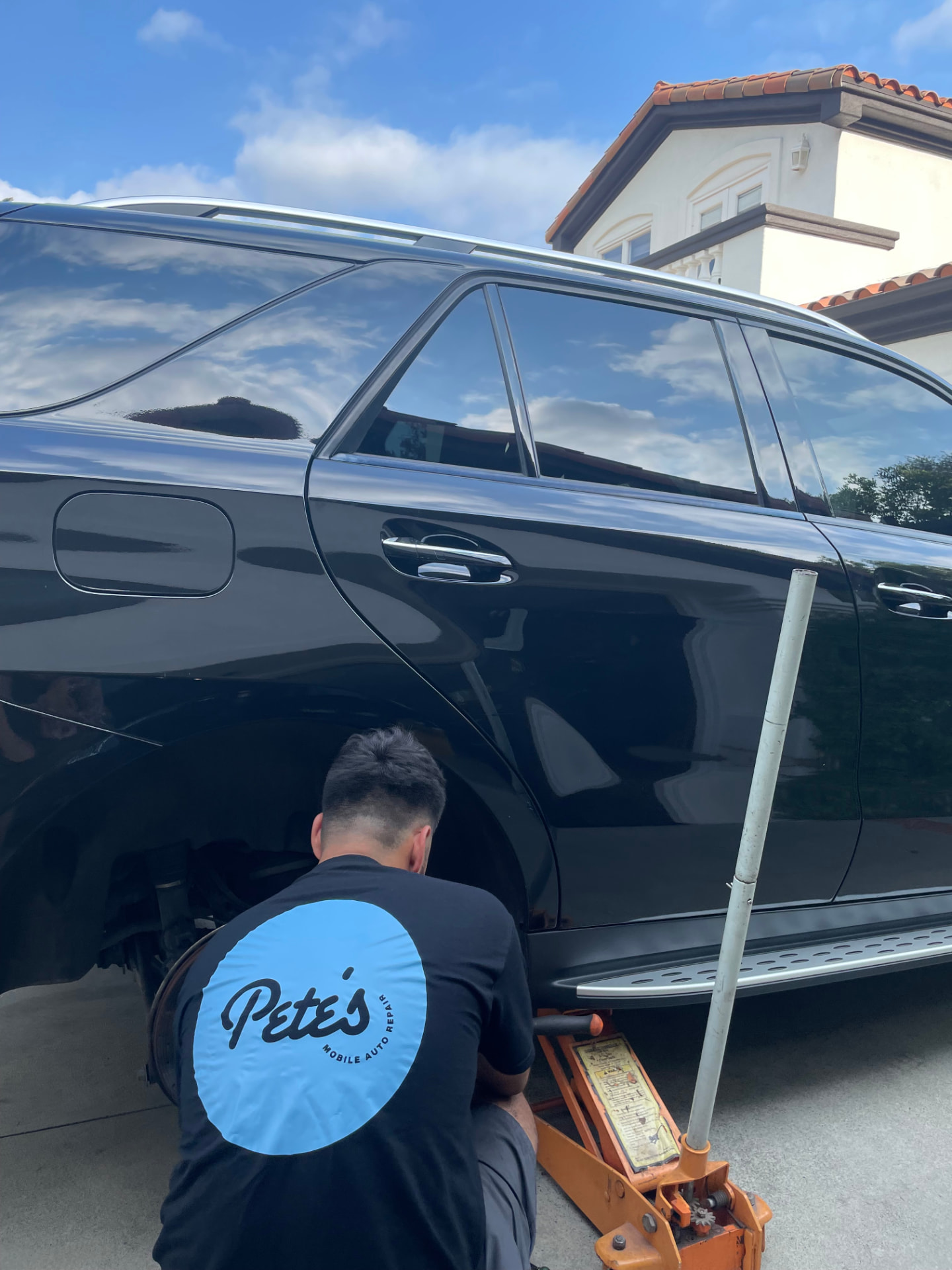 Pete's technician servicing a black SUV on a jack in a customer's driveway